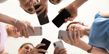 Diverse,Young,Women,Standing,Together,In,Circle,Holding,Smartphones,Looking